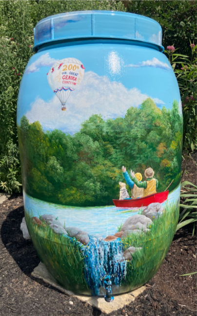 Photo of painted rain barrel with stream and red boat.